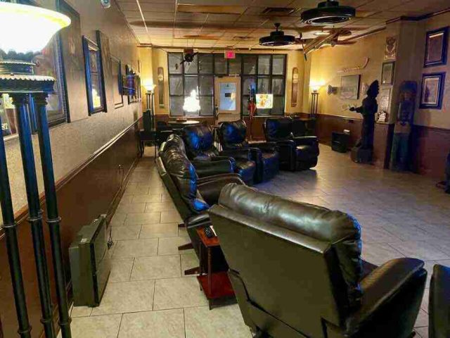 membership-lounge - 10 Rows of comfortable black leather recliner chairs inside the spacious, warmly lit lounge area at F&M Cigars, featuring tiled floors, wood-paneled walls, and classic decor.
