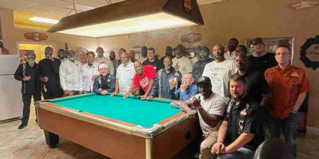 membership-lounge - 12 A large group of diverse patrons and members smiling and posing together around the pool table during a community event inside the F&M Cigars lounge.