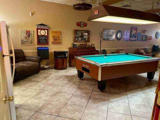 membership-lounge - 4 The public lounge area at F&M Cigars featuring a regulation pool table under a large hanging light fixture, tiled flooring, comfortable leather seating, and wall decor.