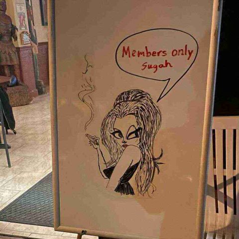 membership-lounge - 8 A hand-drawn whiteboard sign in the lounge entryway featuring a stylized cartoon illustration of a woman smoking a cigar with a speech bubble that reads "Members only Sugah."