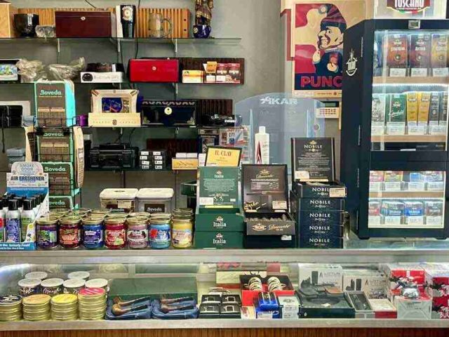 walk-in-humidor - 1 The main retail checkout counter at F&M Cigars, featuring a glass display case with premium cutters and lighters, wall shelving stocked with accessories, and advocacy posters.
