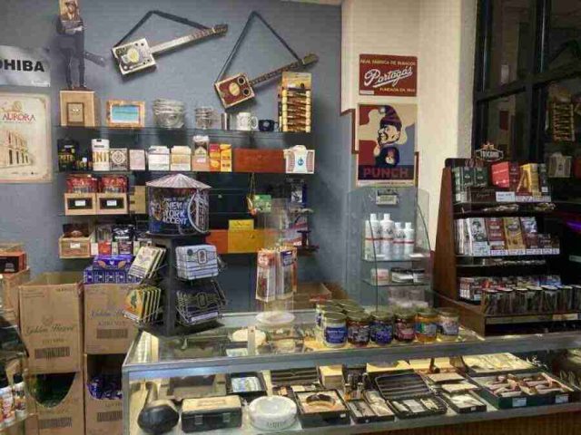 walk-in-humidor - 14 The main retail checkout counter at F&M Cigars, featuring a glass display case with premium cutters and lighters, wall shelving stocked with accessories, and advocacy posters.