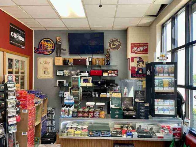 walk-in-humidor - 7 The main retail checkout counter at F&M Cigars, featuring a glass display case with premium cutters and lighters, wall shelving stocked with accessories, and advocacy posters.