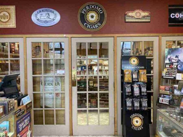 walk-in-humidor - 8 Inside the walk-in humidor at F&M Cigars, featuring fully stocked wooden shelves displaying an extensive selection of premium boutique and classic cigar brands.